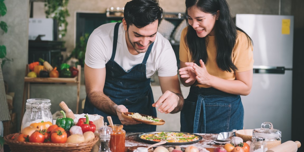 A man and woman couple smile as they prepare a healthy home cooked meal in the kitchen