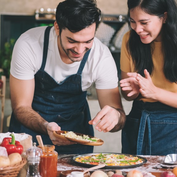 A man and woman couple smile as they prepare a healthy home cooked meal in the kitchen
