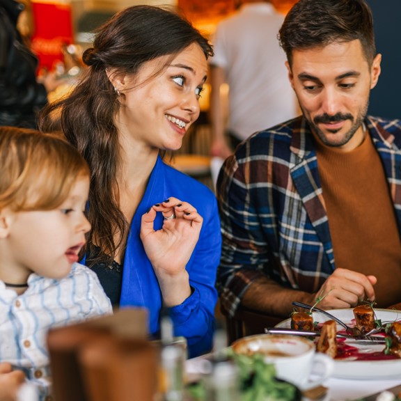 A couple with a young child enjoys a festive meal dining at a restaurant for a special occasion