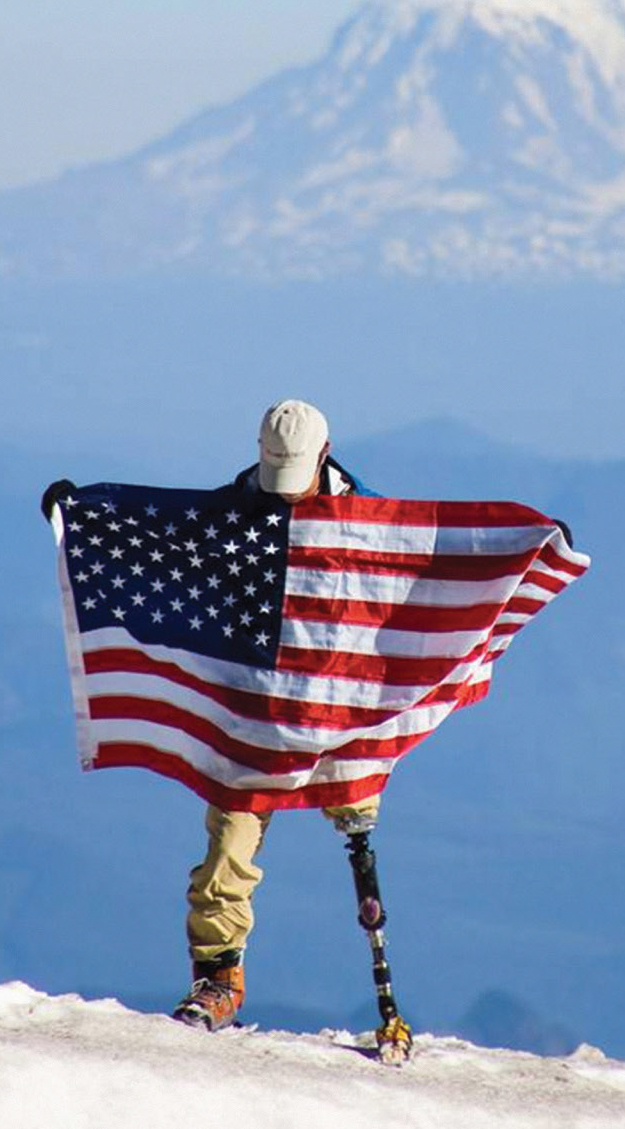 Wounded Warrior holding US flag while standing on snowy mountainside