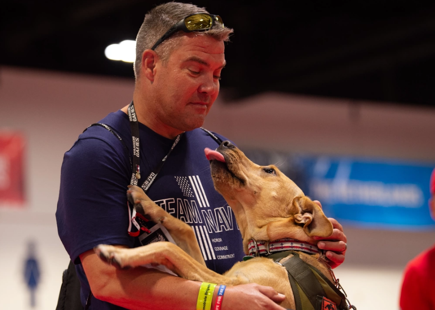 190625-N-PS962-0015 TAMPA, Fla. (June 25, 2019) – Team Navy member Cmdr. Robert Fry hugs his service dog at the 2019 Department of Defense (DoD) Warrior Games, June 25. Team Navy is comprised of athletes from Navy Wounded Warrior-Safe Harbor, the Navy’s sole organization for coordinating the non-medical care of seriously wounded, ill and injured Sailors and Coast Guardsmen, providing resources and support to their families. (U.S. Navy photo by Mass Communication Specialist 3rd Class Petty Officer Louis Thompson Staats IV)