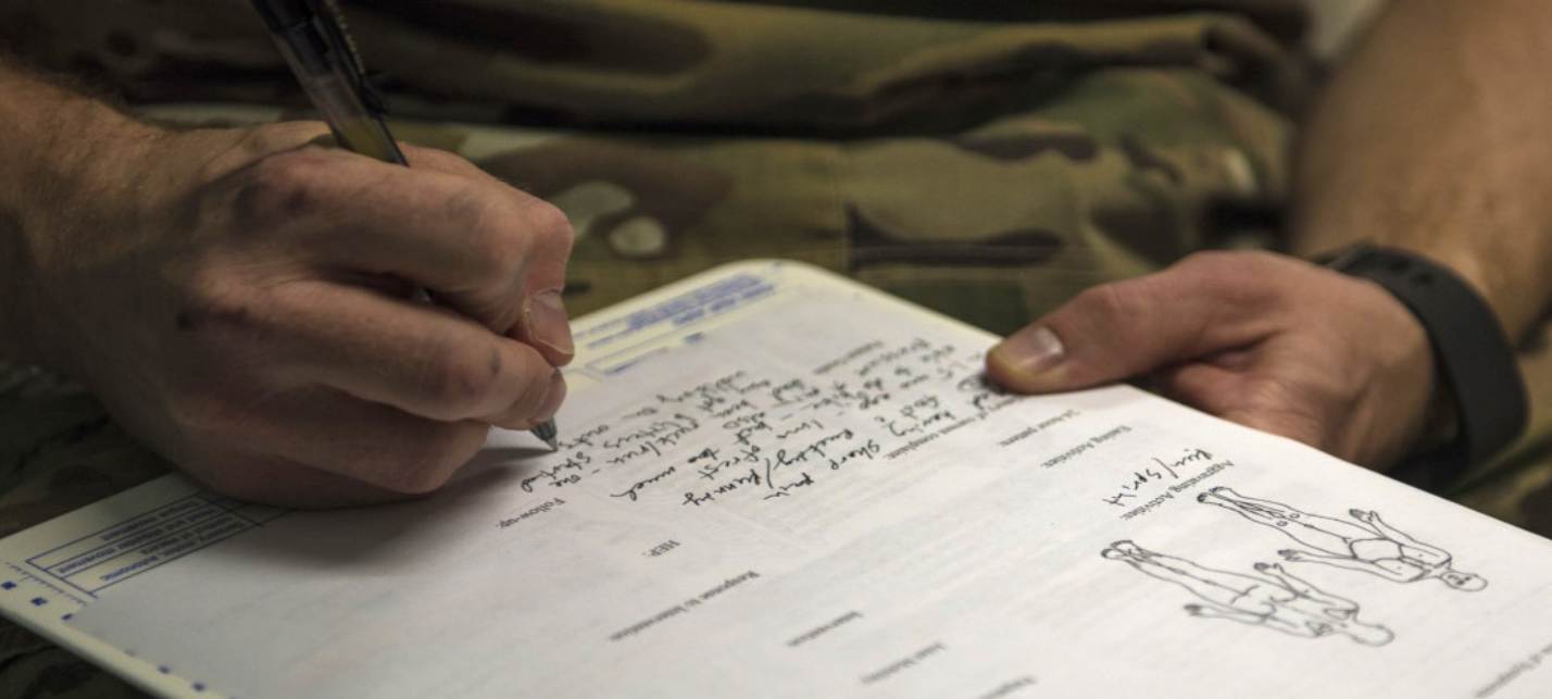 Military doctor charting medical exam and writing patient notes,